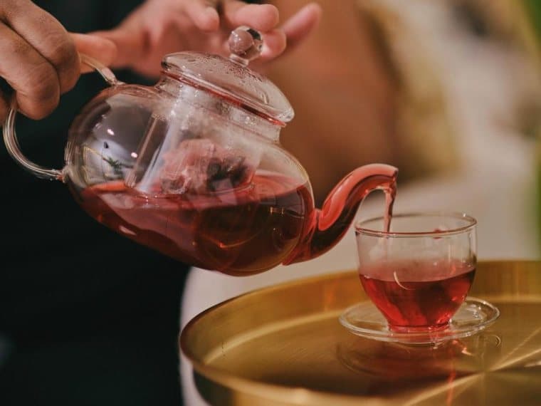 Hibiscus tea being poured into a glass cup on a gold tray